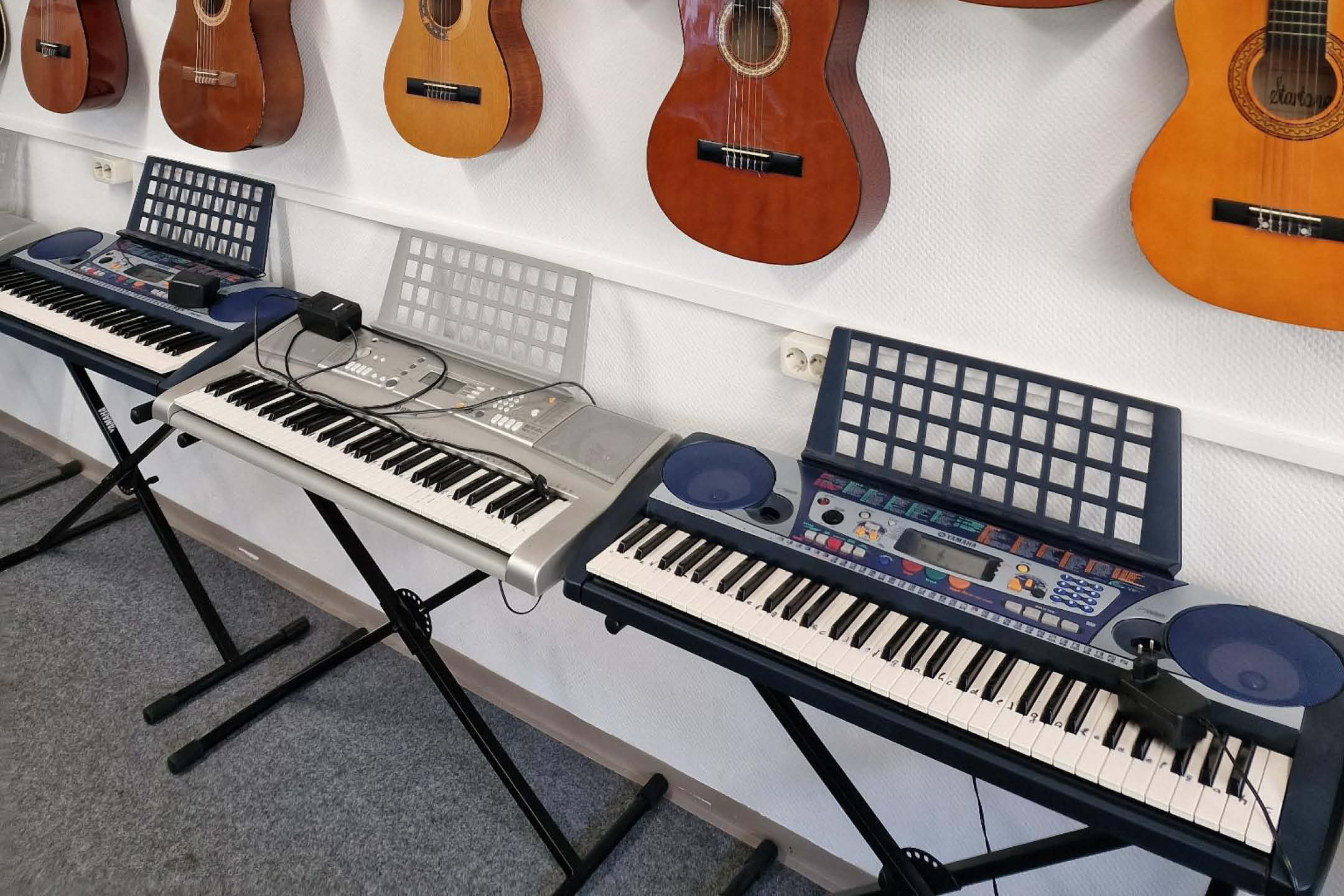 Ein Bild auf dem 3 Keyboards nebeneinander, vor einer Wand stehen.